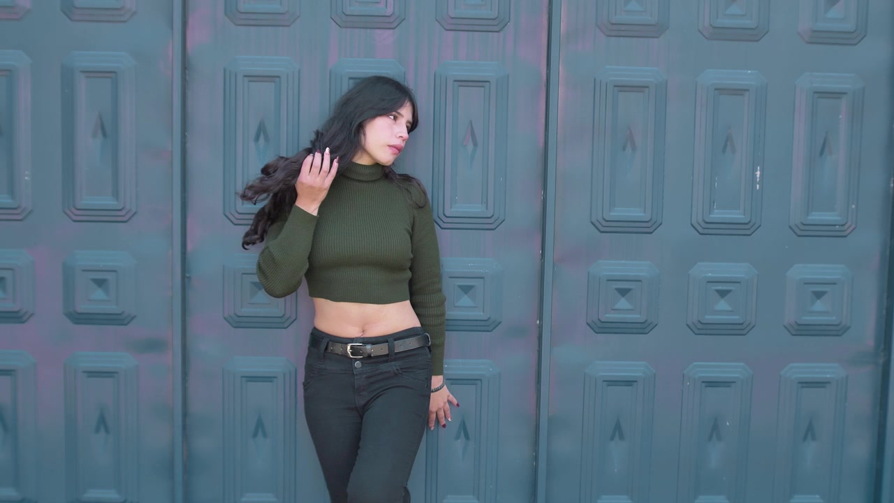 Young brunette woman posing against textured blue door touching her hair