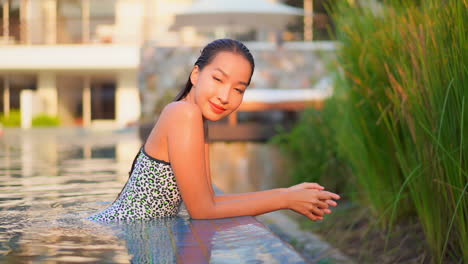 close-up of a pretty young woman leaning along the edge of a resort swimming pool