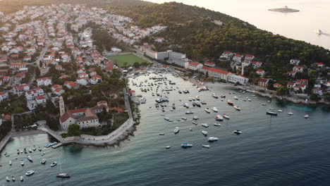 Vista-Aérea-De-Barcos-Flotando-En-El-Océano-Tranquilo-Con-Monasterio-Franciscano-Y-Ciudad-Costera-En-La-Isla-De-Hvar,-Croacia