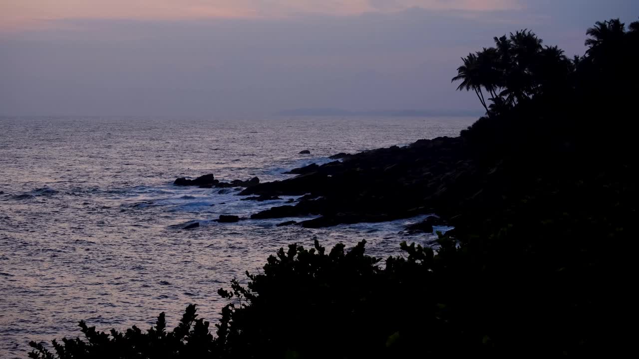 Scenic view of silhouetted rocky coastline with coconut palm trees and ocean waves in southern Sri Lanka