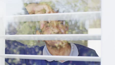 Video-of-thoughtful-senior-biracial-man-leaning-and-looking-out-of-window