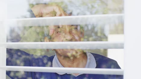video de un hombre biracial senior pensativo inclinado y mirando por la ventana