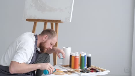 a young artist sits at home on a stool in front of a canvas and works with inspiration paints a