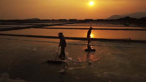 traditional salt makers preparing their field silhouetted against the golden setting sun