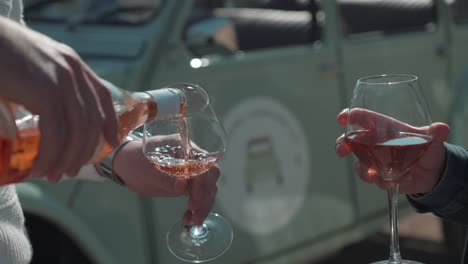 slow motion shot of hands pouring rose wine into glasses in front of a deux chevaux