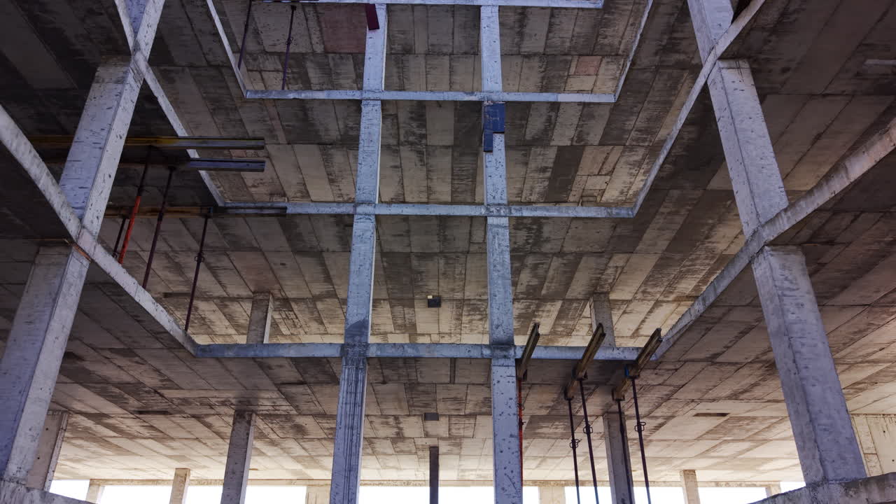 Perspective view of unfinished building with visible slabs, columns, and scaffolding. Interior view of multi-level concrete structure. Aerial