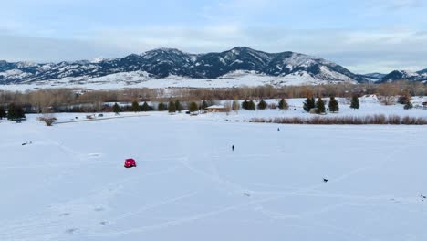 Vuelo-Aéreo-De-Boseman-Montana-Sobre-Un-Parque-Suburbano-Nevado-A-La-Hora-Dorada,-Drones-De-4k-Sobre-Pescadores-De-Hielo-Y-Trineos-Con-Fondo-De-Montaña