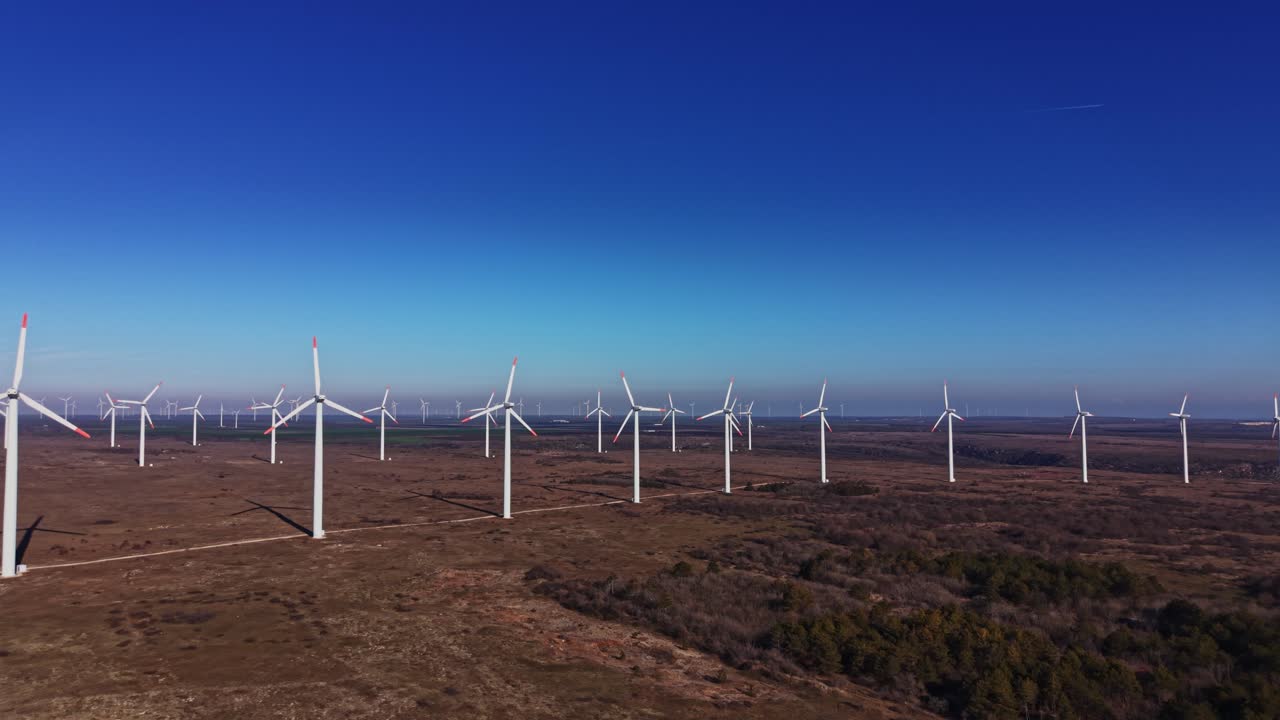 Aerogeneratori torreggiano in un paesaggio remoto sotto un cielo blu terso