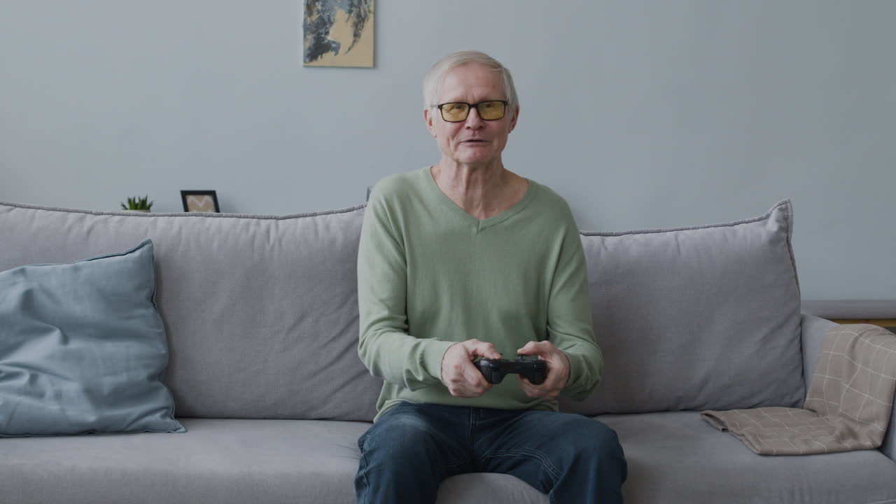 lycklig äldre man som spelar videospel medan han sitter på soffan hemma