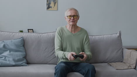 Glücklicher-älterer-Mann,-Der-Videospiel-Spielt,-Während-Er-Zu-Hause-Auf-Dem-Sofa-Sitzt