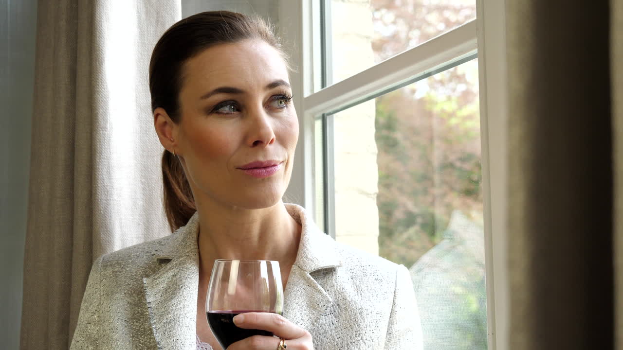 Close up attractive, classy white caucasian woman holding glass of wine looking out window