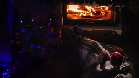 a man admires the fire in the fireplace next to christmas decorations