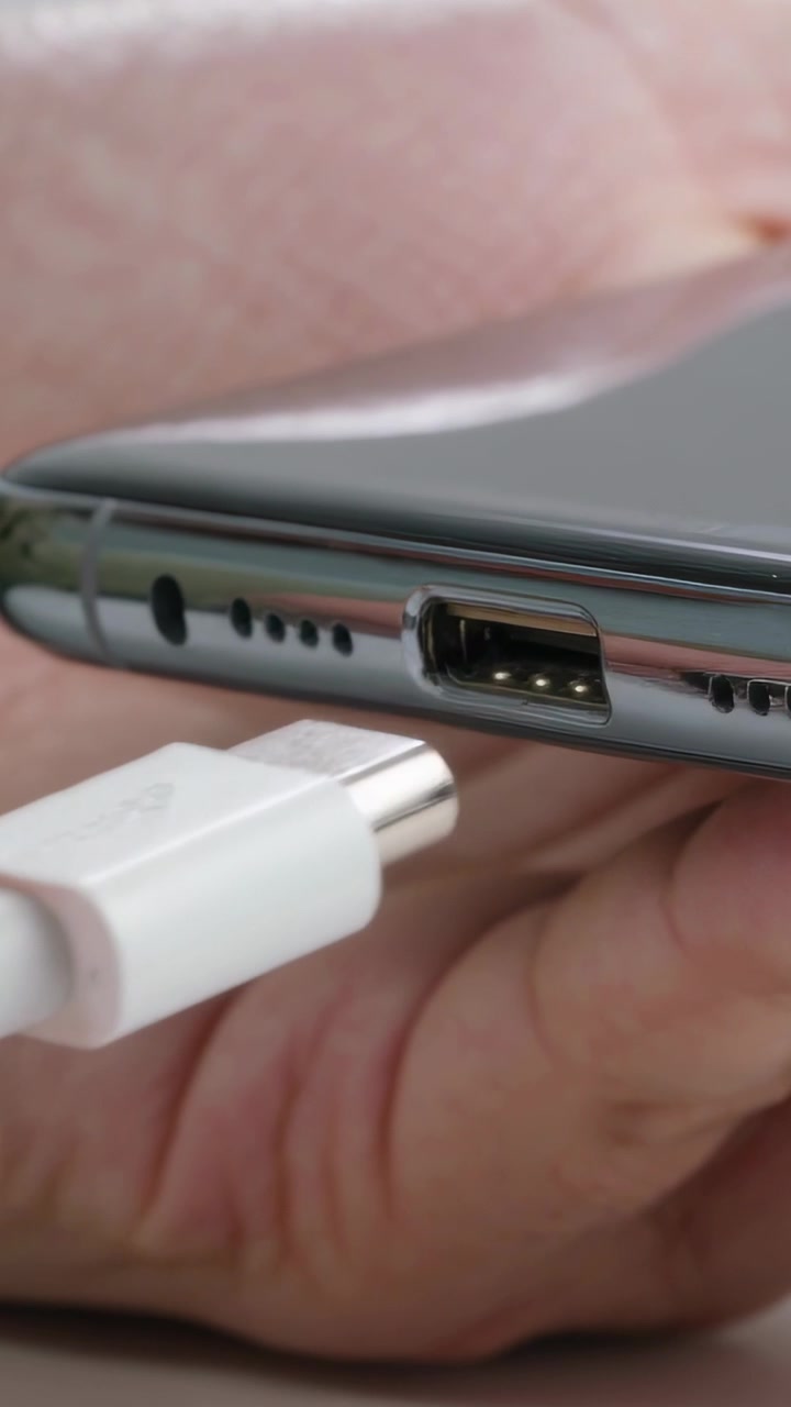 Vertical video: Approaching hand guiding USB-C connector into phone port on table, charging device