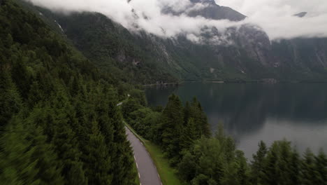 Aerial-View-of-Road-Along-Eikesdalsvatnet-Lake-in-Norway-With-Mountainous-Nature-Scenery-and-Low-Lying-Clouds