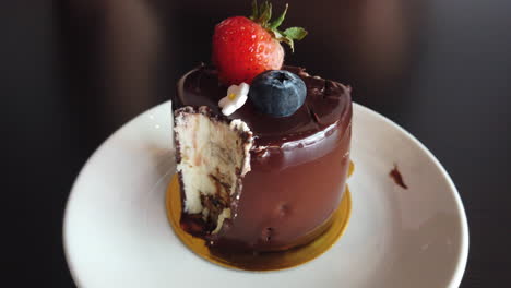 A-yummy-looking-mini-chocolate-cake-on-white-plate-with-blue-berry-and-strawberry-as-toppings-with-man-forking-it