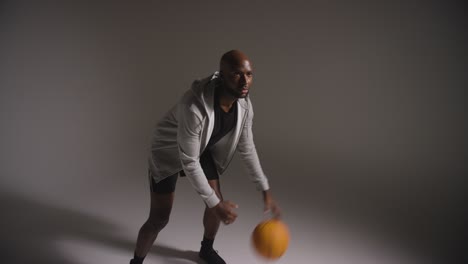 studio shot of male basketball player dribbling and throwing ball against dark background