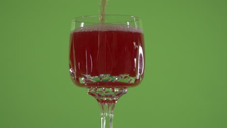 red liquid pouring into fancy spinning glass in front of chroma green screen