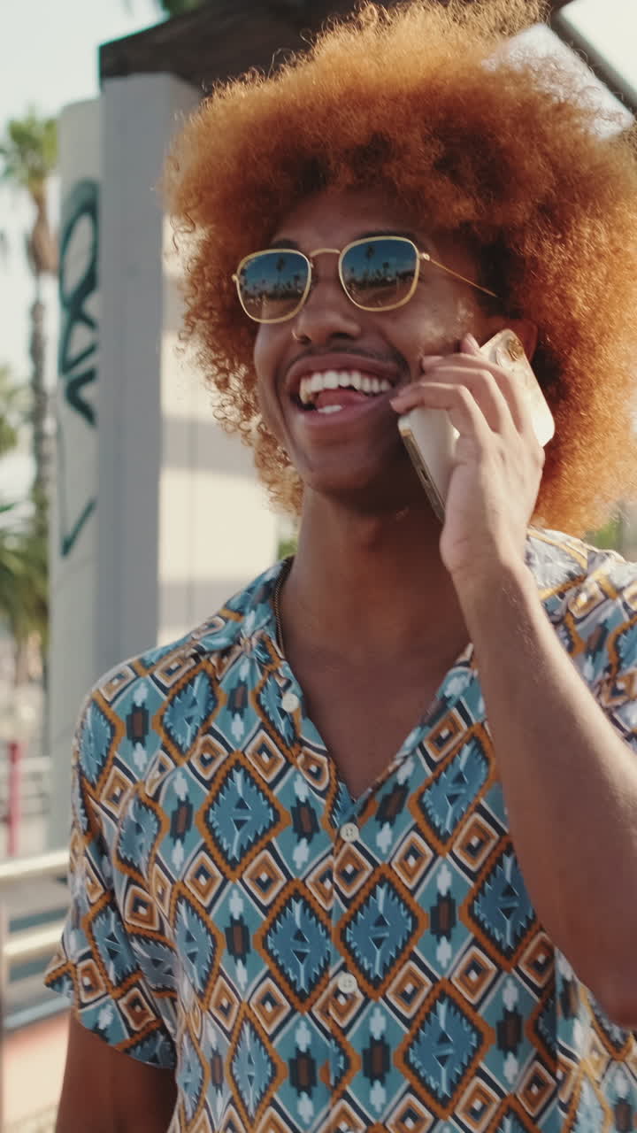 Giovane uomo allegro con capelli afro che ride mentre parla al telefono.