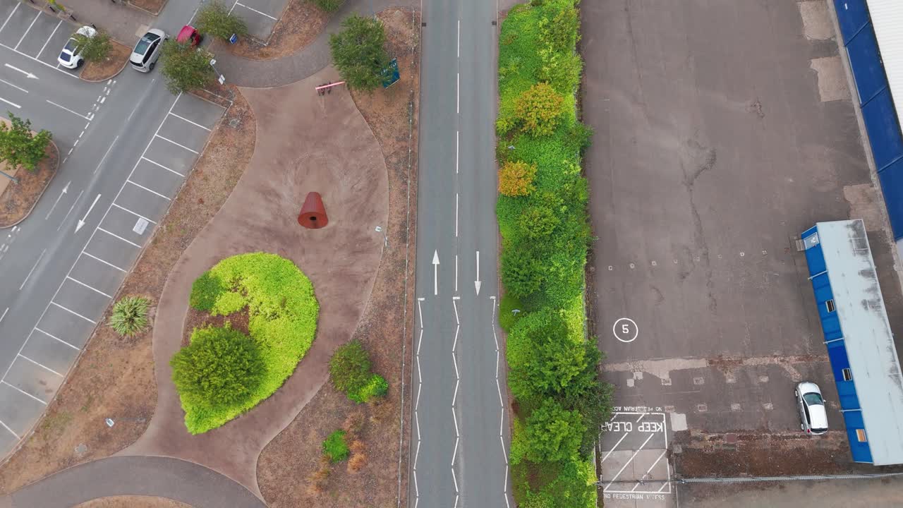 An aerial view of a roundabout with distinct lane markings and curbside parking. The scene includes buildings, sidewalks, and vegetation, showcasing urban planning
