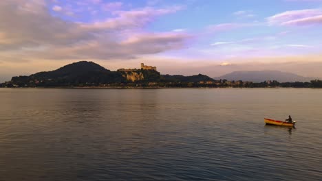 fisherman slowly rowing small fishing boat on calm lake waters of maggiore lake in italy