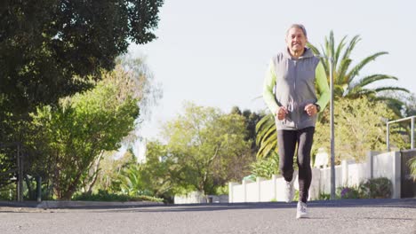 Video-of-smiling-senior-biracial-man-in-sports-clothes-running-on-sunny-street