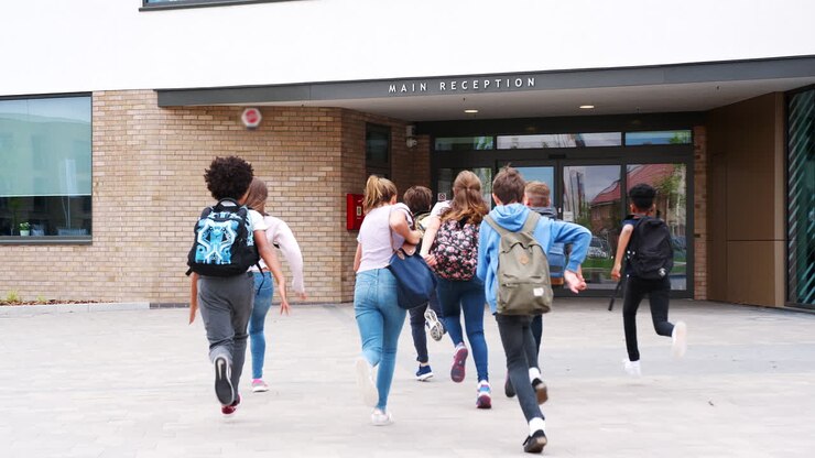Group Of High School Students Running Into School Building At Beginning Of Class
