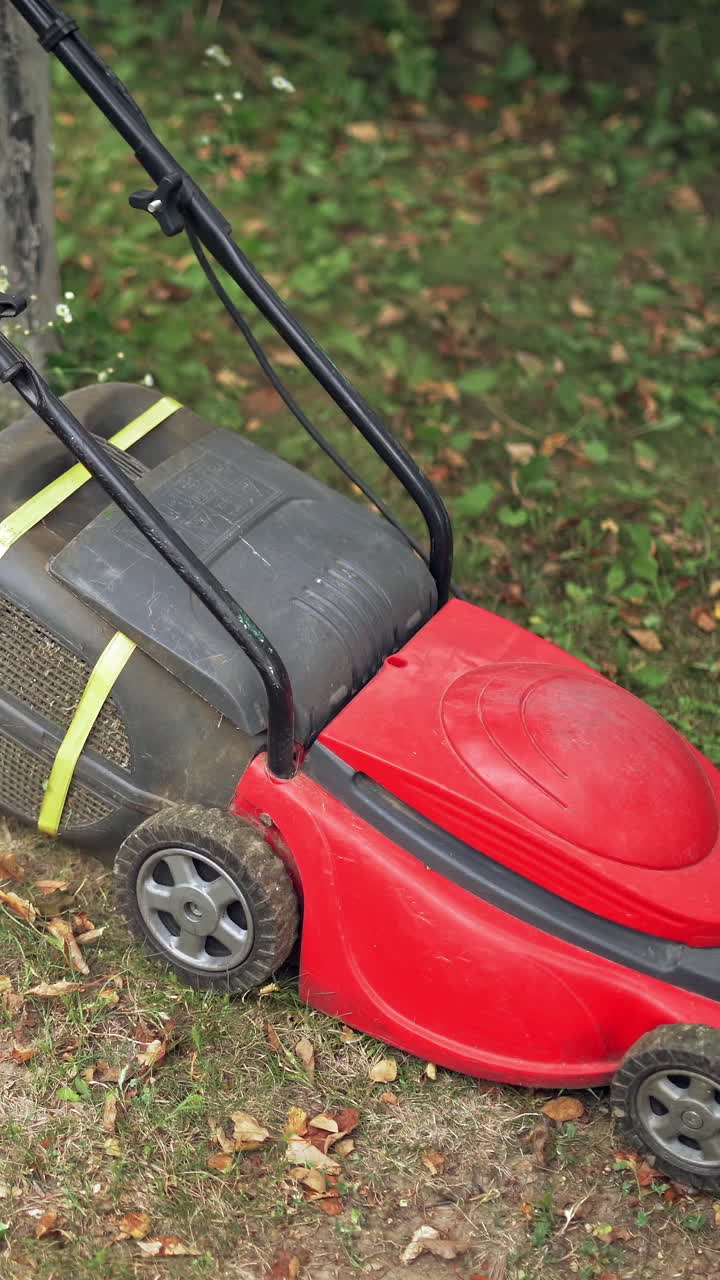 Electric lawn machine during work. Worker is cutting grass in the backyard in summer. Gardening activity. Vertical video