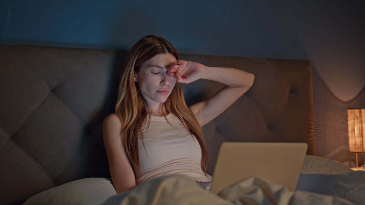 Tired woman working bed typing laptop keyboard. Serious lady feeling sleepless