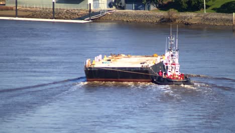 a tug boat manoeuvres an empty flat deck barge down a river