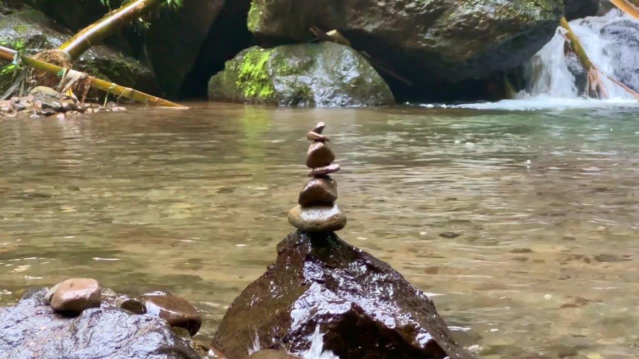 Sassi in equilibrio su una roccia di fiume con sfondo di cascata, concetto di natura serena per benessere e meditazione.