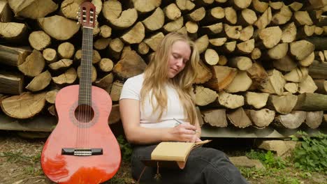 Female-guitarist-songwriter-composes-chords-and-lyrics-by-rustic-logs