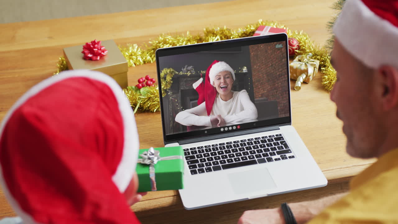 padre y hijo caucásicos con sombreros de santa usando una computadora portátil para una videollamada de navidad con una mujer en la pantalla