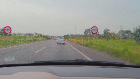 Grains-of-rain-drops-on-the-windscreen-making-incredible-view-while-driving-on-the-highway-of-Mallorca,-Spain-having-lush-greenery-around-in-rainy-weather