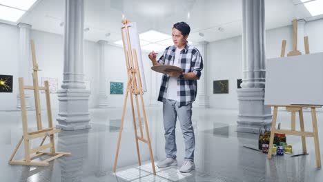 cuerpo lleno de artista masculino asiático sonriendo y mostrando un gesto de paz a la cámara mientras pinta en lienzo con pinturas al óleo y pincel en la galería