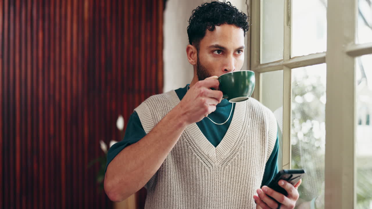 Man using phone and drinking coffee by window