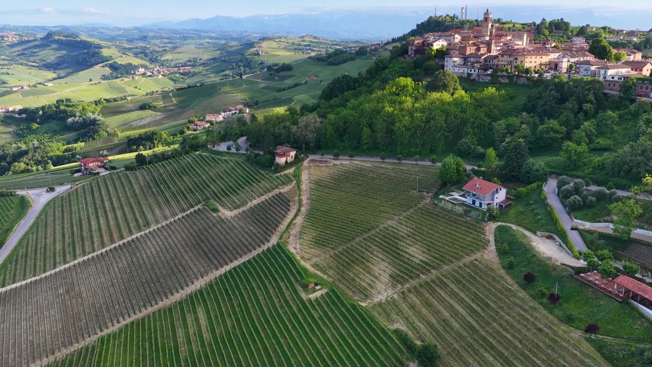 Riprese drone catturano dolci vigneti verdi e un borgo storico in collina sotto un sole splendente