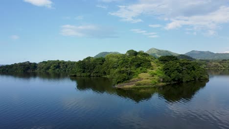 Aerial-approaching-shot-of-green-vegetated-Rainforest-and-lake-with-mountains-in-background-during-sunny-day---Biosphere-natural-reserve-of-Los-tuxtlas