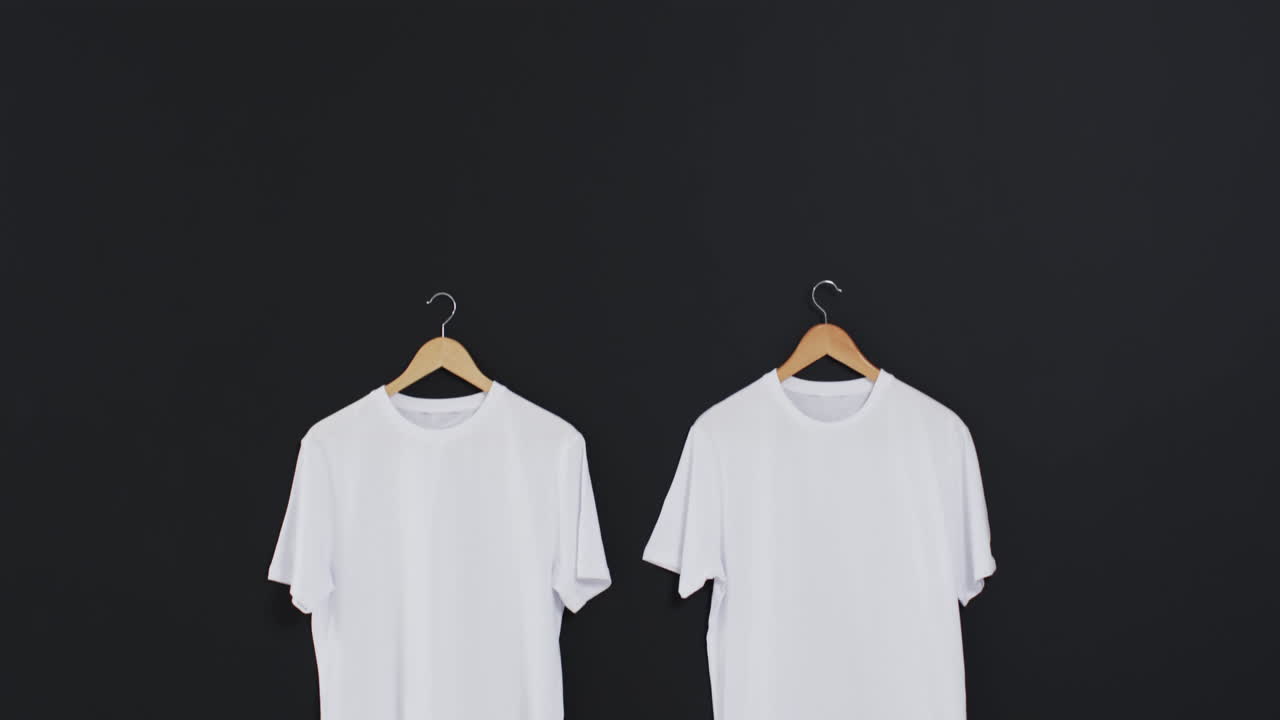 Video of two white t shirts on hangers and copy space on black background