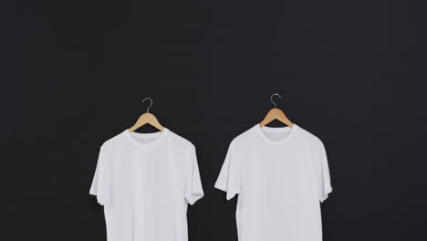 video of two white t shirts on hangers and copy space on black background