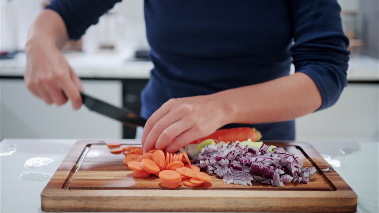 Woman cutting up a carrot near other vegetables on a wooden cutting board