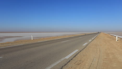 camino vacío del desierto que se extiende hacia el horizonte bajo un cielo azul claro, tunisia