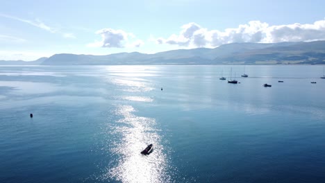 Snowdonia-clear-mountain-range-aerial-panning-right-view-across-sunny-calm-Welsh-shimmering-seascape