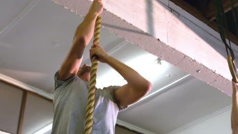 fit man climbing rope in gym