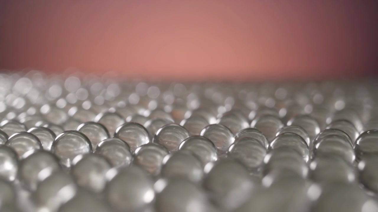 Pulling focus, camera operator moving focus deeper across glass beads in studio showing color shift