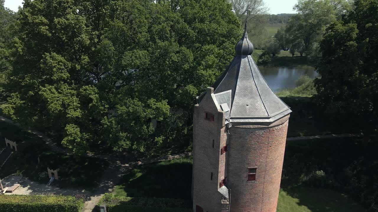 Drone fly by of a small magical tower of Castle Loevestein with birds flying over on a bright sunny day in the Netherlands