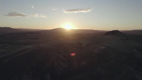 Drone-flying-over-Italian-landscape-with-hills,-trees-and-fields-of-grass,-straight-towards-the-sunrise-in-4k