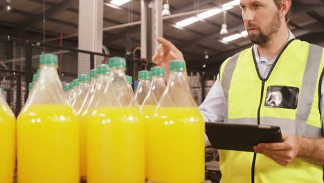 trabajador que mantiene un registro en una tableta digital mientras cuenta las botellas