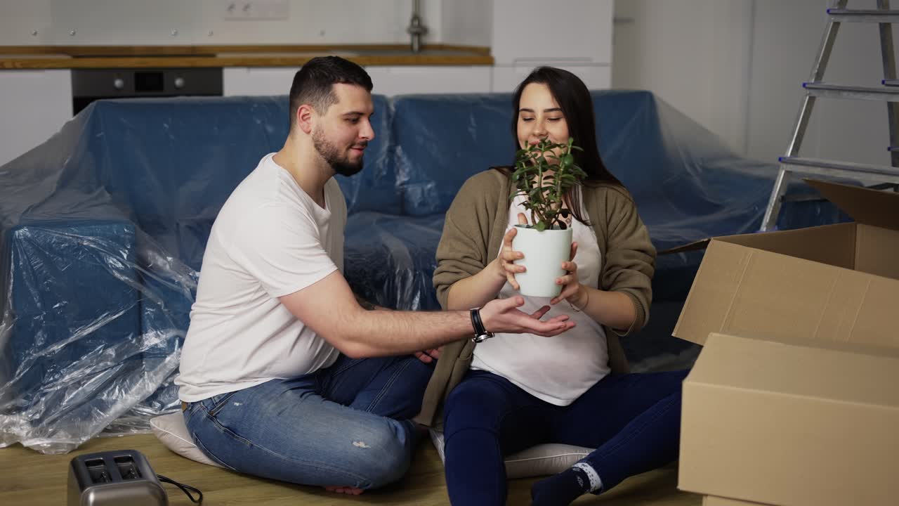Happy young couple sitting on the floor in the living room, unpacking stuff