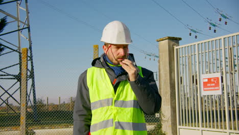 Ingeniero-Masculino-Con-Gafas-De-Sol-En-Su-Chaleco-Reflectante-De-Seguridad-Mientras-Está-De-Pie-En-La-Subestación-Eléctrica,-Dinámico-De-Mano