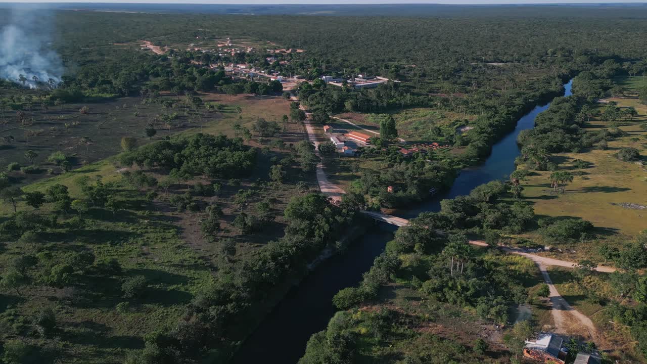 Inquadrature a media altitudine di un drone del corridoio fluviale del Cerrado: acqua blu perenne e tortuosa, foresta a galleria ripariale circostante, infrastrutture di insediamento, aree agricole in mezzo alla vegetazione circostante
